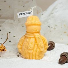 a yellow candle with a sign that says scented candle next to some brown acorns