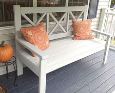 a white bench sitting on top of a wooden porch next to a window with pumpkins