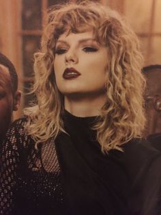 a woman with long blonde hair and red lipstick standing next to a man in black