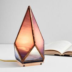 an open book sitting on top of a table next to a lamp that is shaped like a pyramid