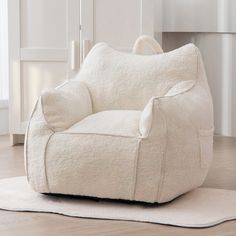 a white chair sitting on top of a wooden floor next to a rug in front of a window