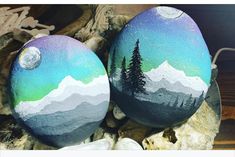 two painted rocks sitting on top of a rock covered in snow and pine tree designs