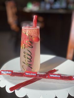 two strawberries in a tall glass on top of a white plate next to some candy bars