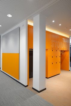 an empty room with orange lockers and white columns on the wall, along with carpeted flooring