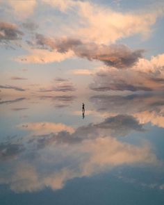 a lone person standing in the middle of a cloud filled sky at sunset or dawn