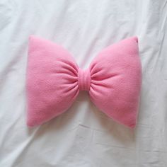 a pink bow tie laying on top of a white bed sheet in the shape of a pillow