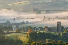 an aerial view of a church surrounded by trees and fog in the valley below it