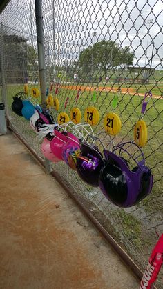 the baseball field is fenced off and has many different colored helmets hanging on it