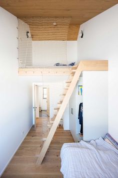 a bed sitting under a wooden staircase next to a white wall in a room with wood flooring