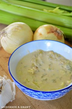 a blue and white bowl filled with soup next to celery, onions and leeks