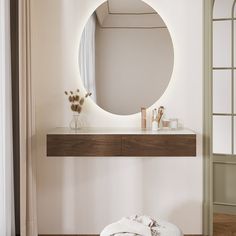 there is a round mirror on the wall above a table with a white towel and vase