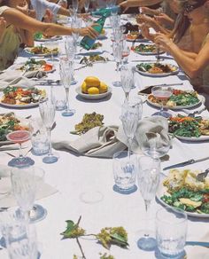 a group of people sitting at a long table with plates of food and wine glasses