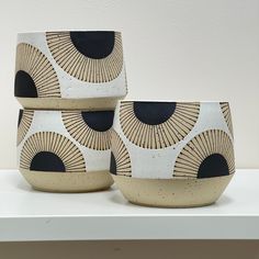 three black and white bowls sitting on top of a table next to each other in front of a wall