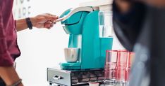 a woman is using a coffee maker on a counter top while another person holds a cup in front of her