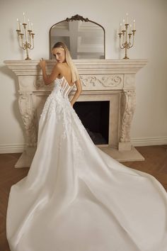 a woman in a white wedding dress standing next to a fireplace with candles on it