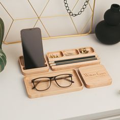 a wooden tray with glasses, cell phone and pen on it next to a black vase