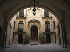 an archway leading into a large building with potted plants on the floor and two chandeliers hanging from the ceiling