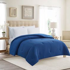 a blue comforter on a bed in a room with white carpet and windows,