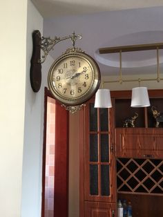 a clock hanging from the side of a wall next to a wine rack and lamp