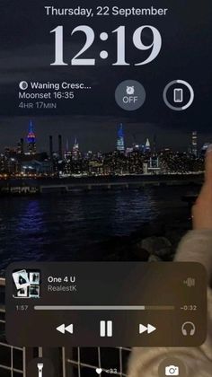 an iphone screen showing the time and weather in new york city at night, as seen from brooklyn bridge