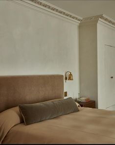 a large bed sitting next to a white wall with a brown pillow on top of it