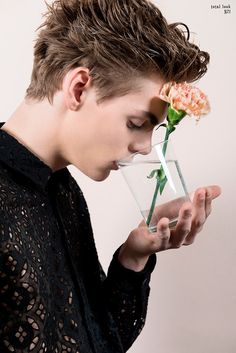 a young man is smelling a flower in a vase with water on his face and looking down at it