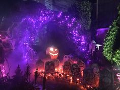 halloween decorations with purple lights and pumpkin heads in the middle of a garden at night