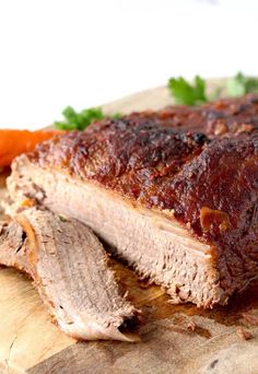 a piece of meat sitting on top of a cutting board next to carrots and parsley