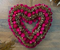 a heart shaped wreath with pom - poms hanging on a wooden floor next to pine cones