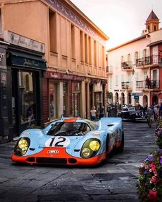 an orange and blue race car parked on the side of a street next to tall buildings