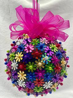 a colorful ornament hanging on a white wall with a pink ribbon and bow