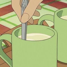 a hand holding a spoon over two mugs filled with milk