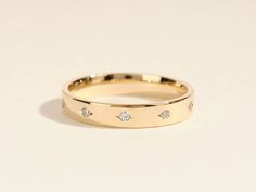 a yellow gold wedding ring with three diamonds on the inside and outside, set against a plain white background