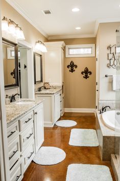 a large bathroom with white cabinets and marble counter tops, along with rugs on the floor