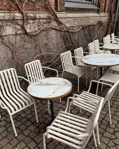 there are many chairs and tables outside on the brick floored area with trees in the background