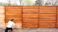 a man in white shirt and black pants spraying water on wooden fence with sprayer