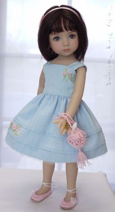 a doll with brown hair wearing a blue dress and holding a pink purse in her hand