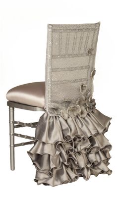 a silver chair with ruffled seat and back cover on it's side, in front of a white background