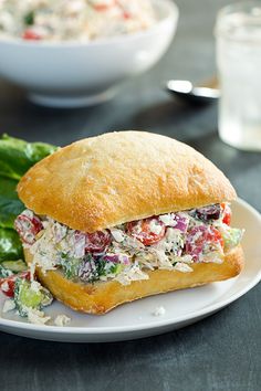 a sandwich on a white plate with lettuce and tomato salad in the background