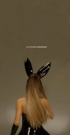 a woman with long hair wearing bunny ears and black latex on her head, standing in front of a gray background