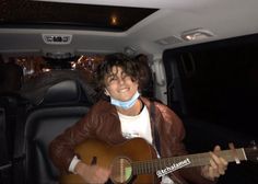 a man sitting in the back seat of a car while holding a guitar and smiling