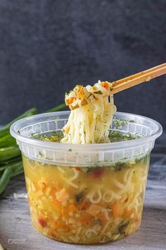 a plastic container filled with noodles and vegetables on top of a wooden table next to green onions