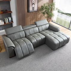 a grey leather sectional sofa sitting on top of a carpeted floor next to a window