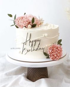 a white cake with pink flowers on top and happy birthday written on the side next to it