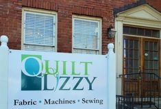 a sign for quilt d'azy in front of a brick building with two windows