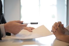 two people sitting at a table with papers and pens in their hands, one holding a pen