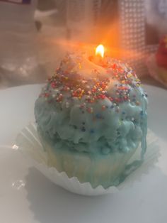 a cupcake with sprinkles and a lit candle in the middle on a plate