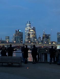 people are standing near the water in front of a cityscape at night time