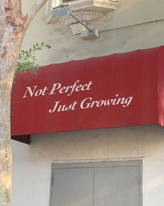 a red sign that says not perfect just growing on the side of a white building