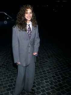 a woman wearing a suit and tie standing in front of a car